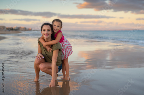 Happy family. Young happy beautiful mother and her daughter having fun on the beach at sunset. Positive human emotions, feelings