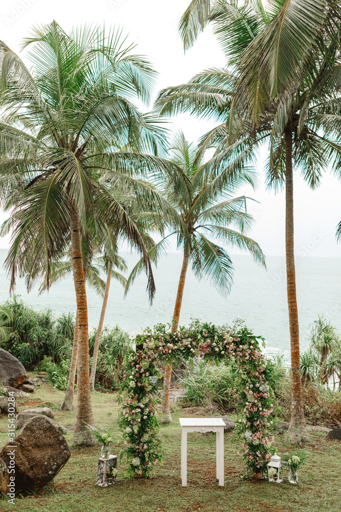 Fototapeta premium Beautiful wedding arch on the tropical beach with palm trees. Beautiful beach wedding venue arrangement in nature in foreground coconut trees with panoramic ocean view