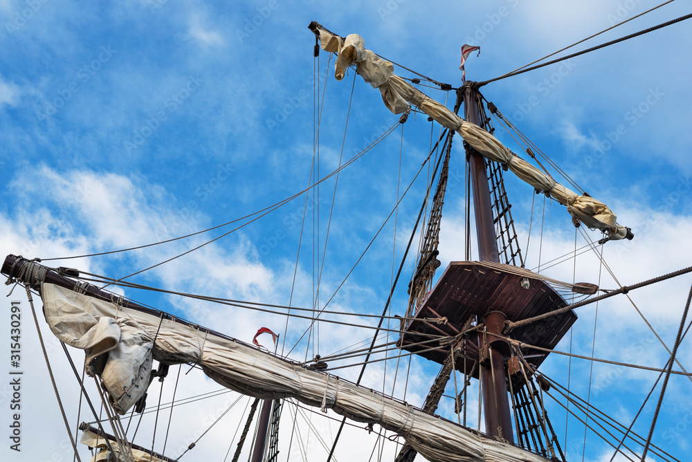 Obraz premium Masts and rigging of old pirate ship on background of cloudy blue sky