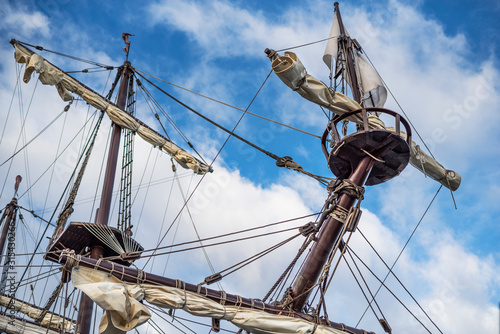 Masts and rigging of old pirate ship on background of cloudy blue sky