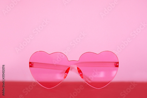 Side view of pink heart shaped glasses on pink and red background