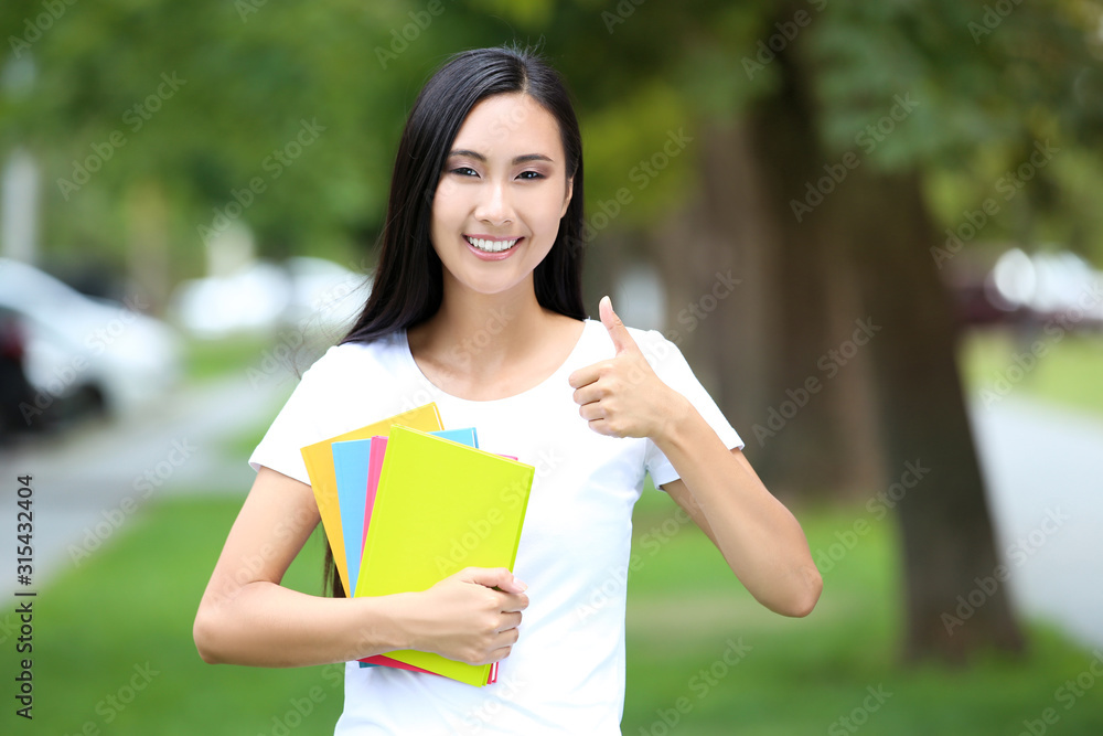 Beautiful young woman with books showing thumb up in the park Beautiful young woman with books showing thumb up in the park