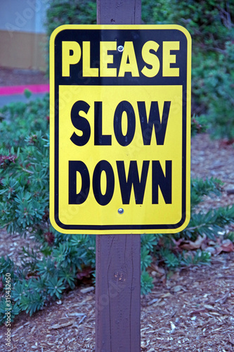 Close-up view of a PLEASE SLOW DOWN sign at the curve of a parking alley