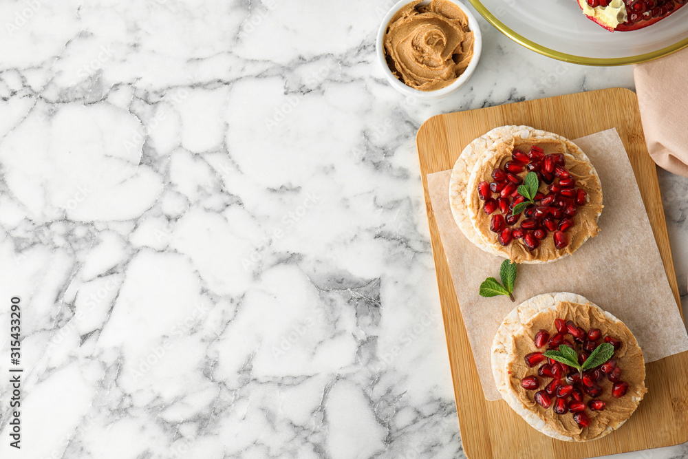 Puffed rice cakes with peanut butter and pomegranate seeds on white marble table, flat lay. Space for text Puffed rice cakes with peanut butter and pomegranate seeds on white marble table, flat lay. Space for text