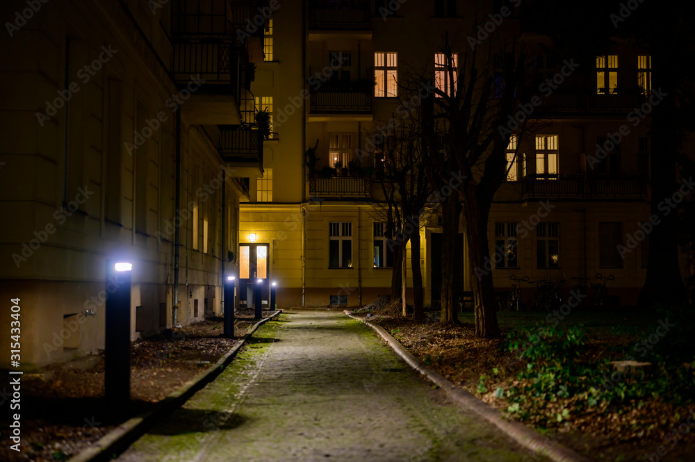 View of the rear building of a residential complex along an illuminated path at night in Berlin, Germany.