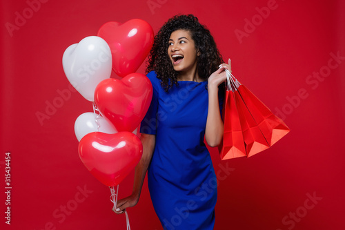 black woman with heart shaped colorful balloons and shopping bags on red background © Anastasia