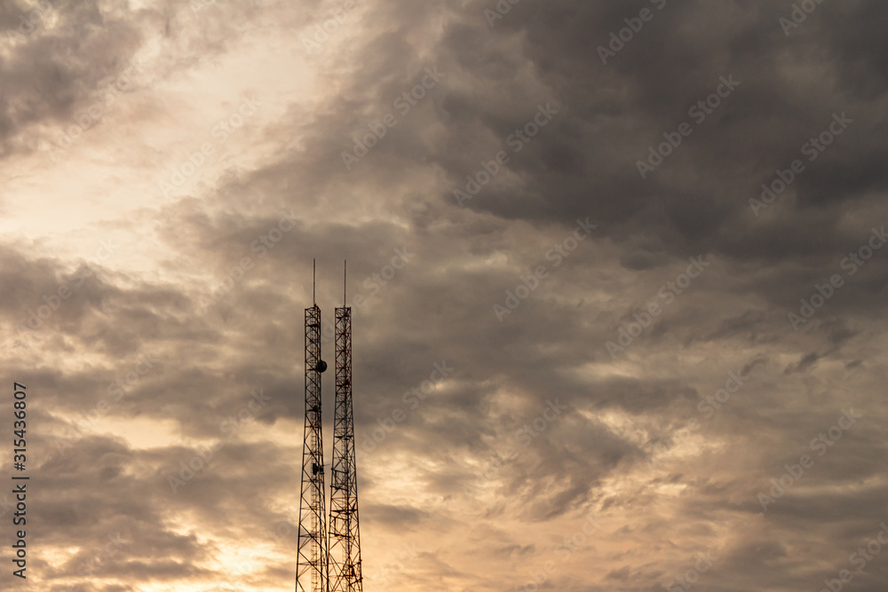 Communications antennas rising towards the cloudy sky. Storm clouds in the sunset. Communications antennas rising towards the cloudy sky. Storm clouds in the sunset.