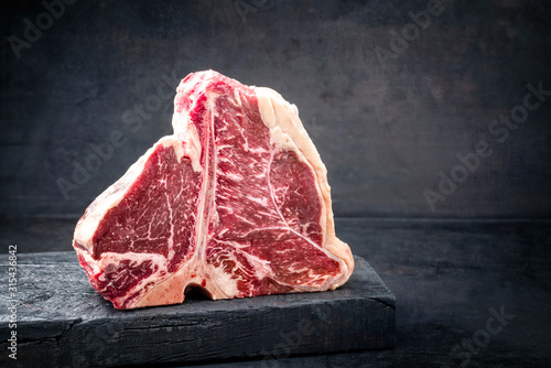 Raw dry aged wagyu porterhouse beef steak with large fillet piece as closeup on a black burnt wooden board with copy space right