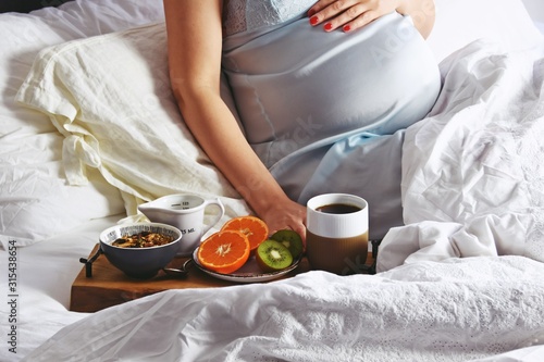 Pregnant woman is having a healthy breakfast in bed. Pregnant woman in a bed on white linen background