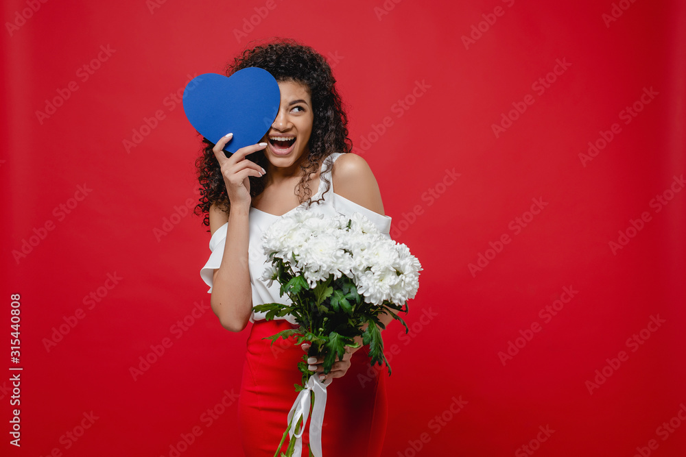 black woman smiling with blue heart shaped valentine card and bouquet of white flowers on red background black woman smiling with blue heart shaped valentine card and bouquet of white flowers on red background