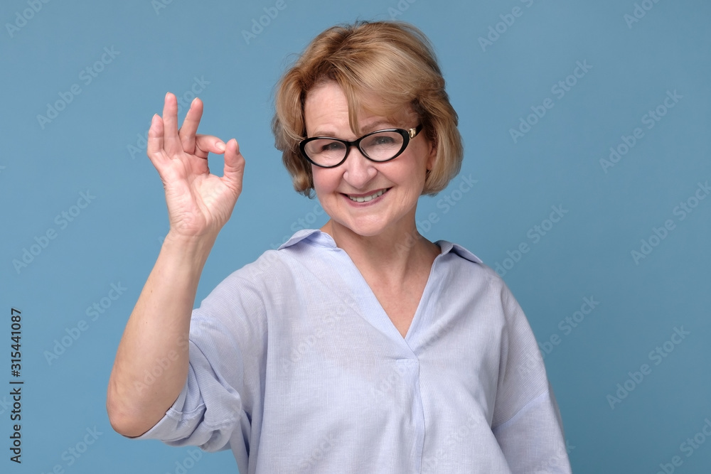 Smiling senior lady in glasses gesturing perfect sign. Teacher approving her students choice