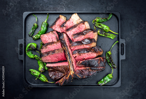 Barbecue dry aged wagyu porterhouse beef steak sliced with large fillet piece with hot chili as top view on a modern design black cast iron tray with copy space