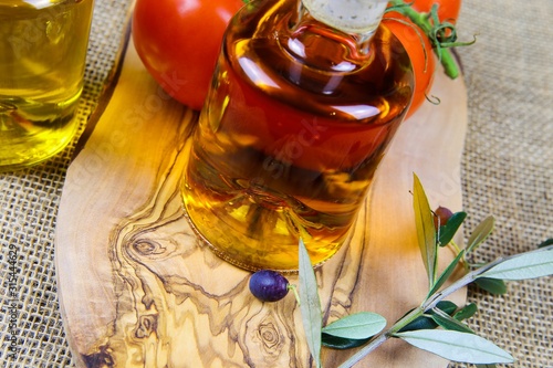 Mediterranean italian healthy food concept: isolated close up of olive oil bottles on wood cutting board with twig and red tomatoes