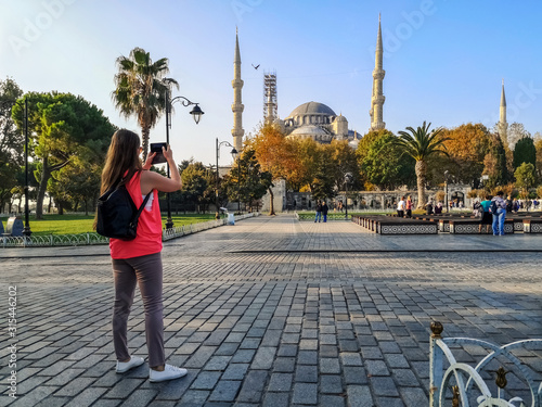 Canvas Print A blonde young tourist woman photographs the Blue Mosque in Istanbul (Turkey) on a smartphone, view from the back