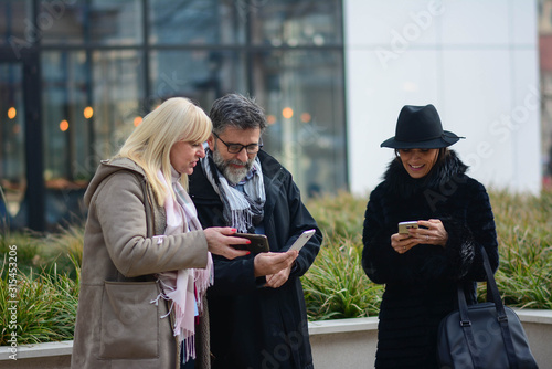 Three colleagues on the break use a smartphone in front of an office building. Colleagues check statuses on social networks at break.