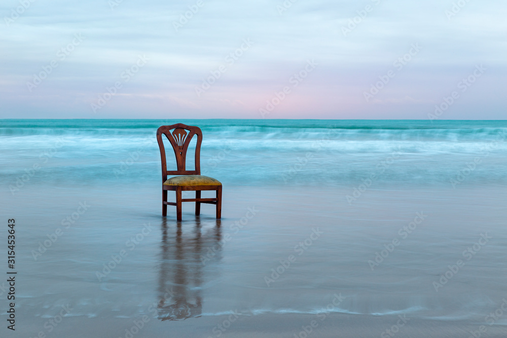 Old chair on the ocean coast, dramatic sky, melancholic scene, loneliness, long exposure
