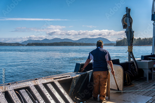 Single fisherman is standing on a commercial crab fishing boat and waiting to pull a pot. Special vessel in Bering sea for catching a king crab. Mountains and forest is on a background. photo
