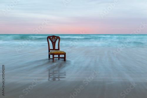 Old chair on the ocean coast, dramatic sky, melancholic scene, loneliness, long exposure