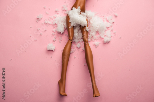 Valokuva plastic doll legs with snow covered  crotch on  pastel pink background