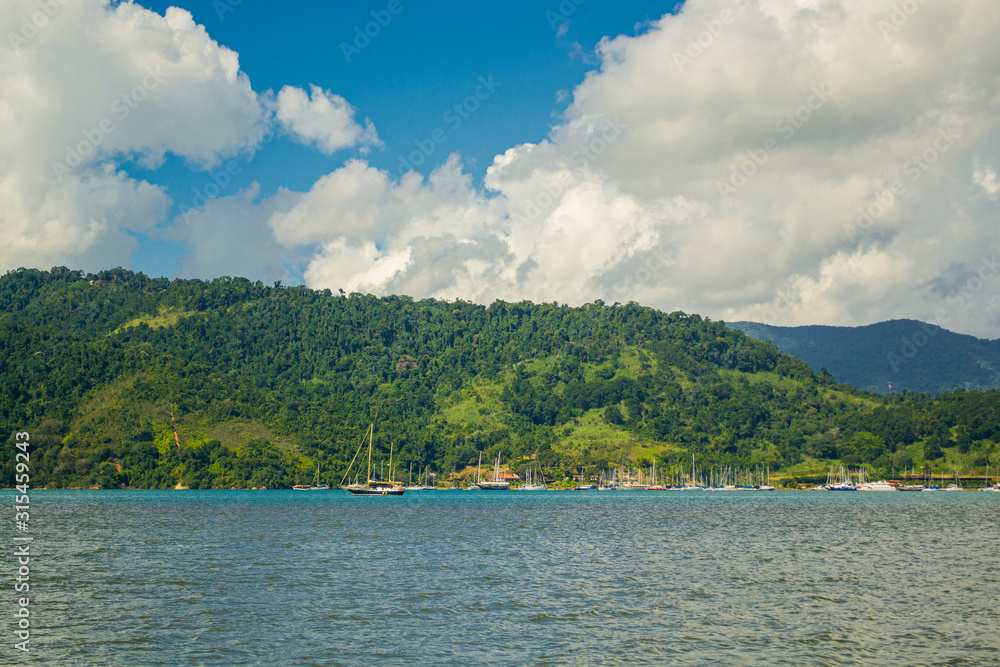 Green mountain covered by trees and surrounded by the ocean with a blue and cloudy sky