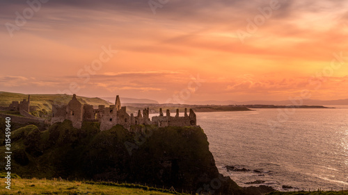 Φωτογραφία Ruined medieval Dunluce Castle on the cliff at amazing sunset, Wild Atlantic Way, Bushmills, County Antrim, Northern Ireland