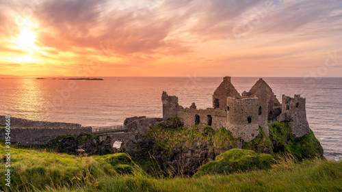 Leinwand Poster Ruined medieval Dunluce Castle on the cliff at amazing sunset, Wild Atlantic Way, Bushmills, County Antrim, Northern Ireland
