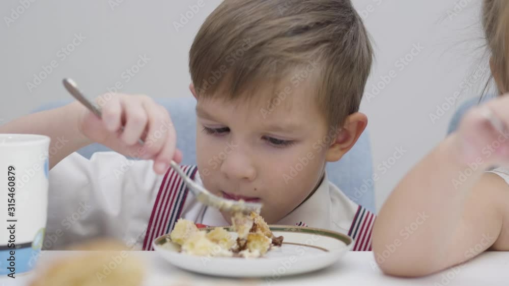 Close-up face of little Caucasian boy eating tasty cake. Cute child sitting at the table and enjoying sweet food. Happiness, leisure, lifestyle. Close-up face of little Caucasian boy eating tasty cake. Cute child sitting at the table and enjoying sweet food. Happiness, leisure, lifestyle.