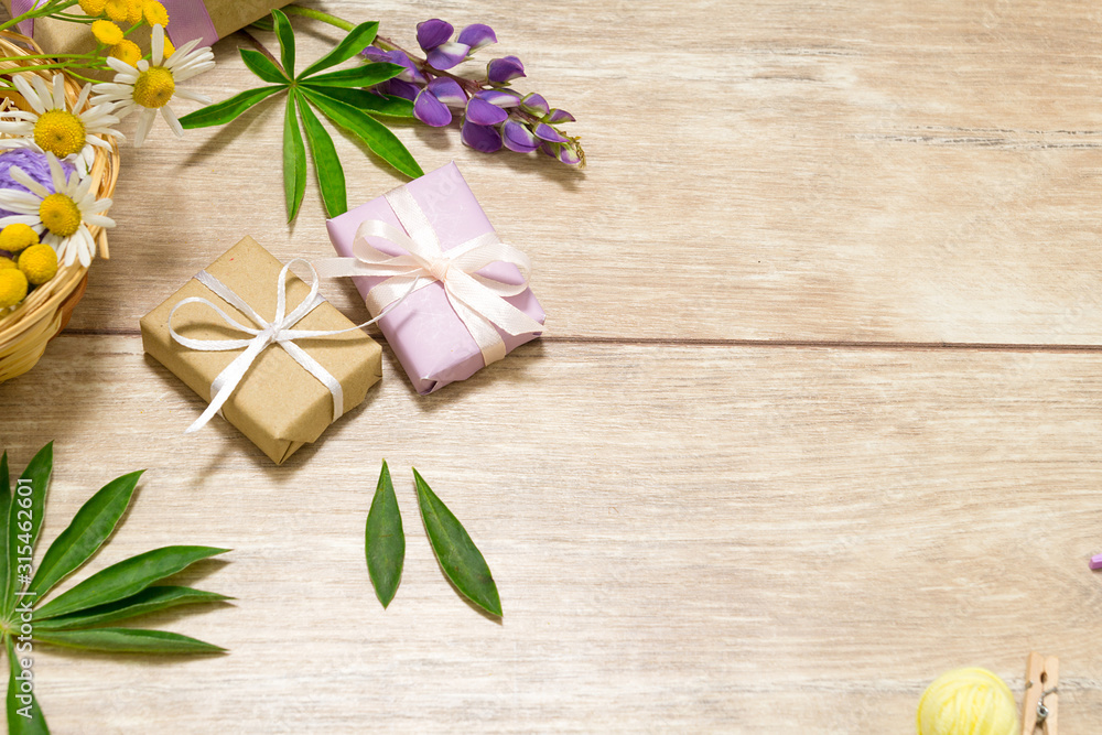 Presents in violet and kraft paper on the wooden table. Purple, white and yellow flowers lay around. Presents in violet and kraft paper on the wooden table. Purple, white and yellow flowers lay around.