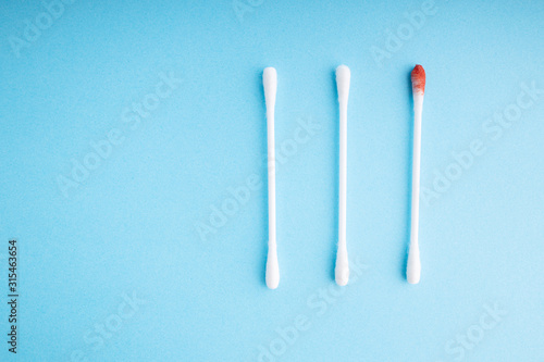 Blood on the hygiene cotton stick. Skincare mockup for design. Menstruation. Stack of disposable cotton stick on a blue background. Cosmetology concept. Bloody wound. Injury. ..