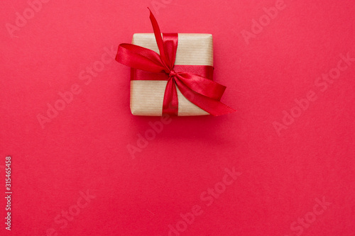 Gift box wrapped with kraft paper and red bow isolated on red background. Abstract flat lay.