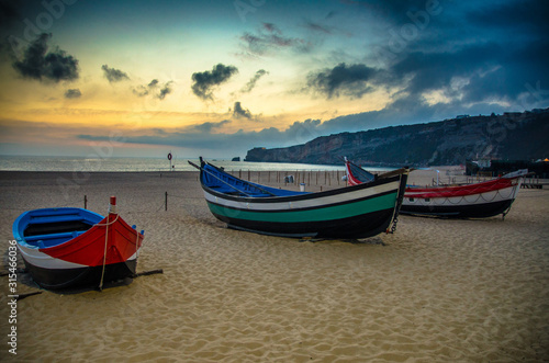 Portugal  Nazare beach  colored wooden boats  panoramic view of Nazare Town  Traditional Portuguese fishing boats in Nazare on the coast  blue clouds on the sky  white sand of  beaches of Portugal