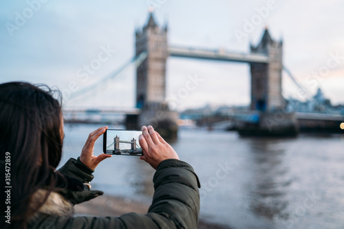 Woman taking a photo with the smart phone to the Tower Bridge in London on a sunny winter day, London, Great Britain. photo