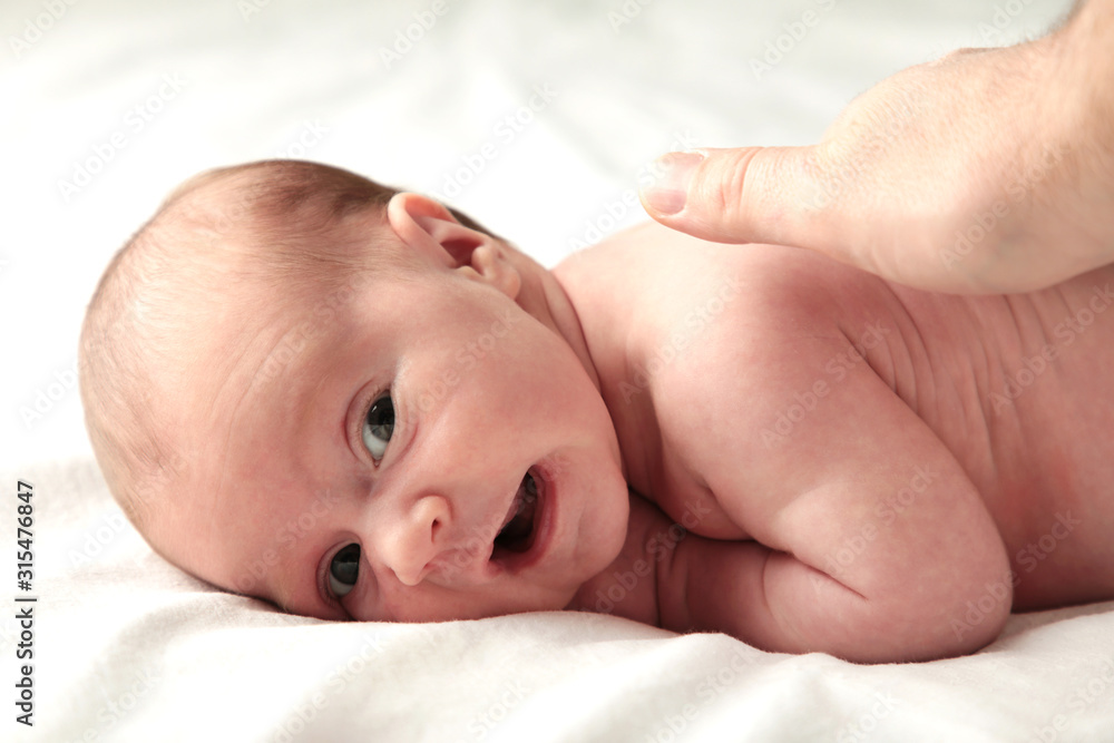 Father's hand stroking a newborn baby on white bed