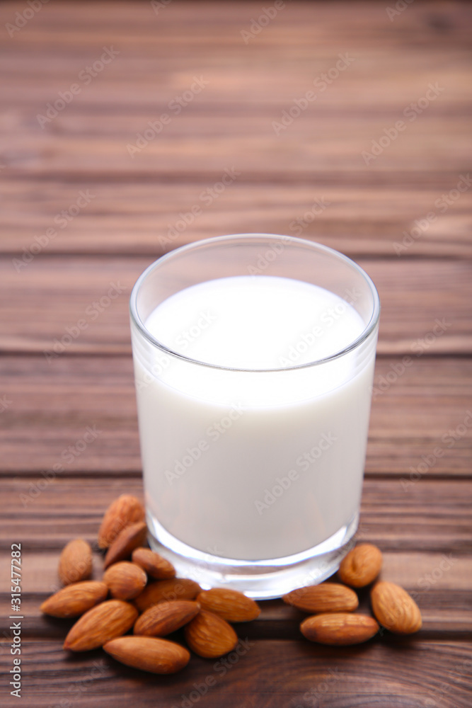 Almond milk in glass with almonds on brown wooden background Almond milk in glass with almonds on brown wooden background