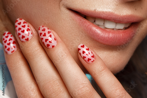 Pretty girl with curls hairstyle, classic makeup, freckles, nude lips and manicure design with hearts. Beauty face. The image for Valentine's Day