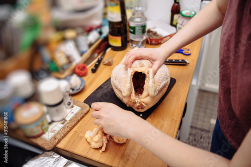 Fotografie Woman removing fat from fresh Capon Chapon cockerel meat on kitchen wooden top F