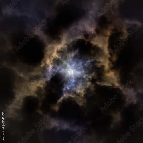 The Moon Partially Covered By Clouds in a Dark Night with Blue, Purple and Brown reflexes