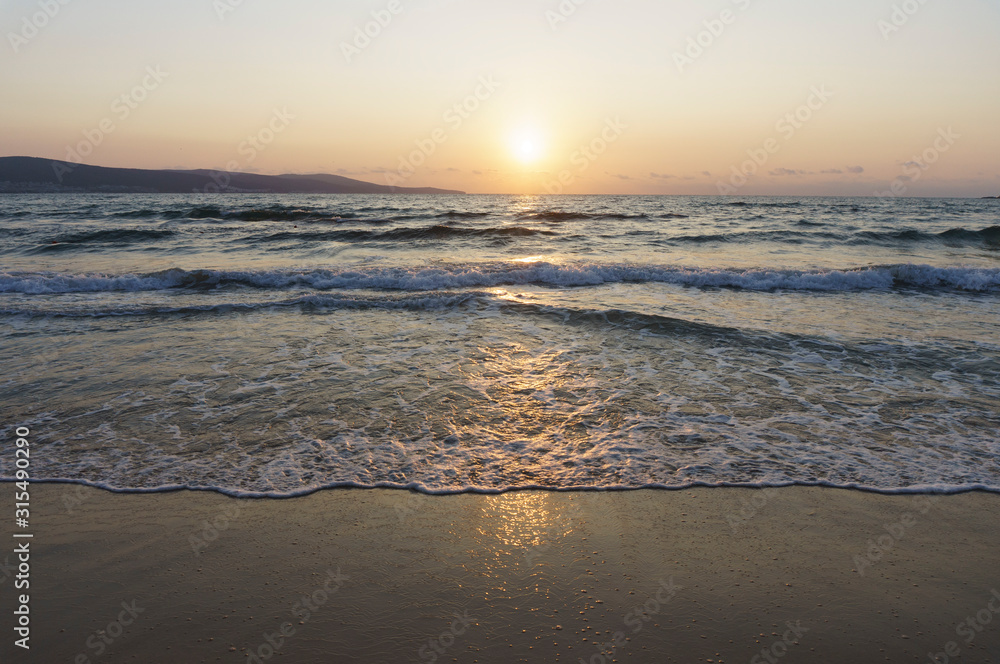 Golden dawn at sea, waves running onto the sand