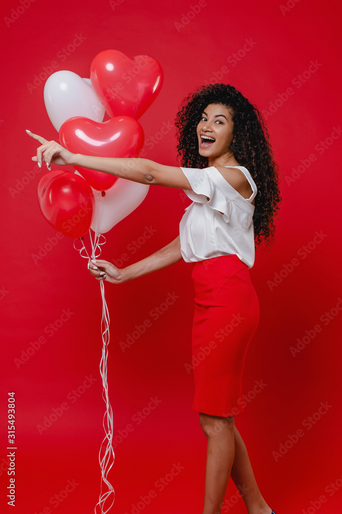 black woman with heart shaped balloons pointing finger on red background black woman with heart shaped balloons pointing finger on red background