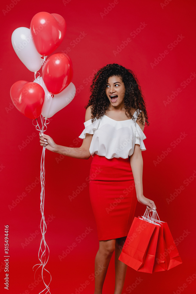 beautiful black woman with colorful heart shaped balloons and shopping bags on red background beautiful black woman with colorful heart shaped balloons and shopping bags on red background