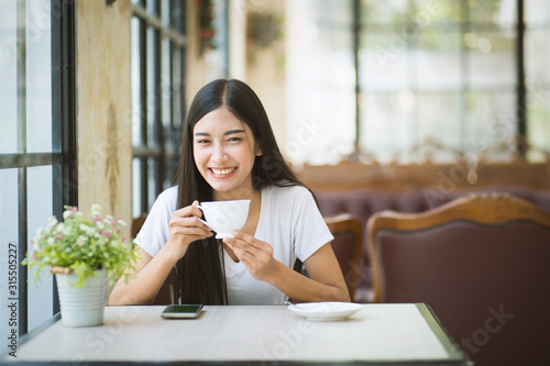 Φωτογραφία A beautiful woman who is sitting drinking coffee near the window with warm sunlight passing through in the morning