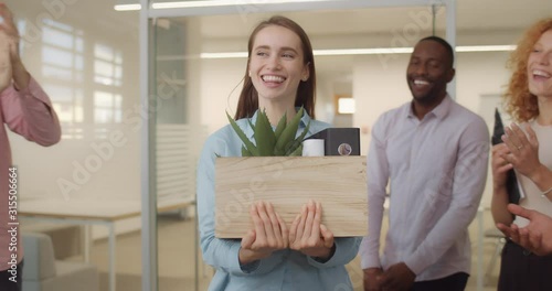 Excited girl trainee getting promotion and walking with things in box. Front view of smilling office workers gratulating woman at first day on new job. Concept of work,career and success.