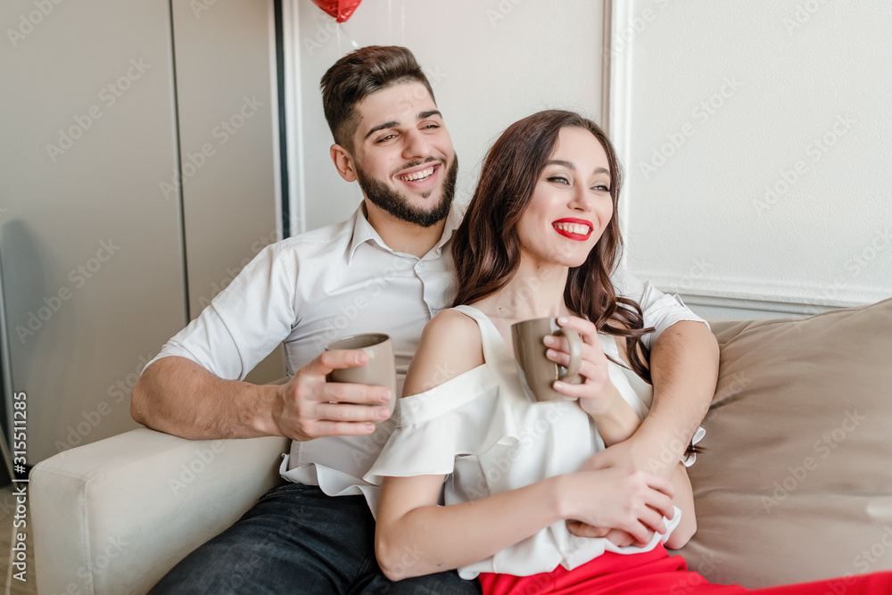 man and woman in love drinking from cups in the morning on couch at home man and woman in love drinking from cups in the morning on couch at home