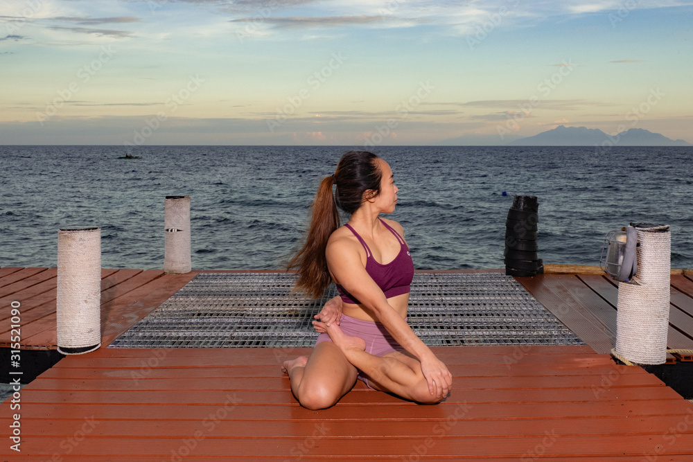 Young beautiful Filipina woman yoga posing on oceanside pierduring tropical sunset 
