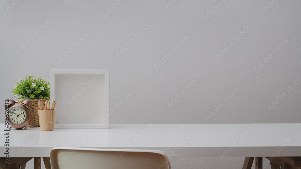 Fototapeta premium Cropped shot of workspace with copy space, decorations, frame and coloured pencils on white table with white wall