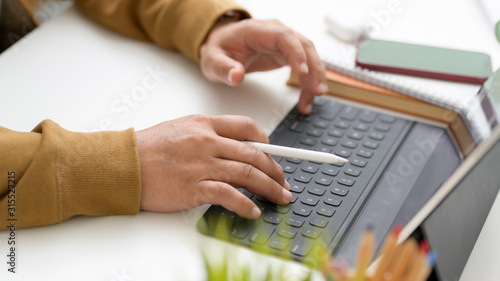 Cropped shot of typing on tablet in simple workspace with office supplies, coloured pencils and tree pot