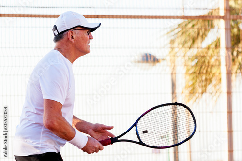 An elderly man plays tennis on an outdoor court © Дворецкая Таня