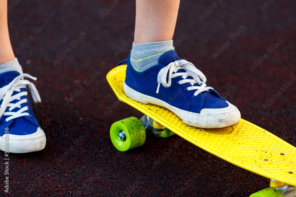 Close up legs in blue sneakers riding on yellow skateboard in motion. Active urban lifestyle of youth, training, hobby, activity concept. Active outdoor sport for kids. Child skateboarding. Close up legs in blue sneakers riding on yellow skateboard in motion. Active urban lifestyle of youth, training, hobby, activity concept. Active outdoor sport for kids. Child skateboarding.