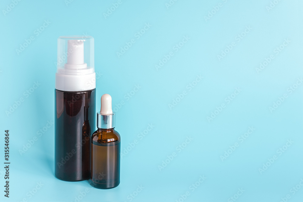 Small brown dropper bottle and big bottle with white dispenser on blue background. Concept beauty cosmetics product. Small brown dropper bottle and big bottle with white dispenser on blue background. Concept beauty cosmetics product.