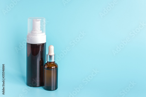 Small brown dropper bottle and big bottle with white dispenser on blue background. Concept beauty cosmetics product.